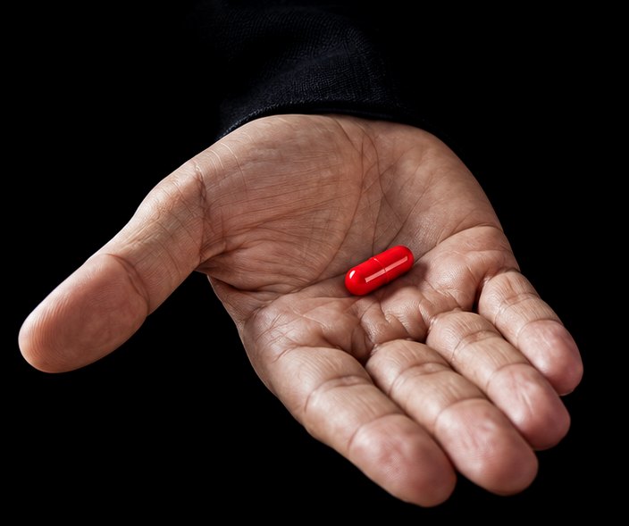 An open hand holding a red capsule